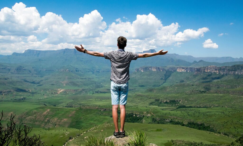 A man stands triumphantly with arms open, overlooking a scenic mountain range.