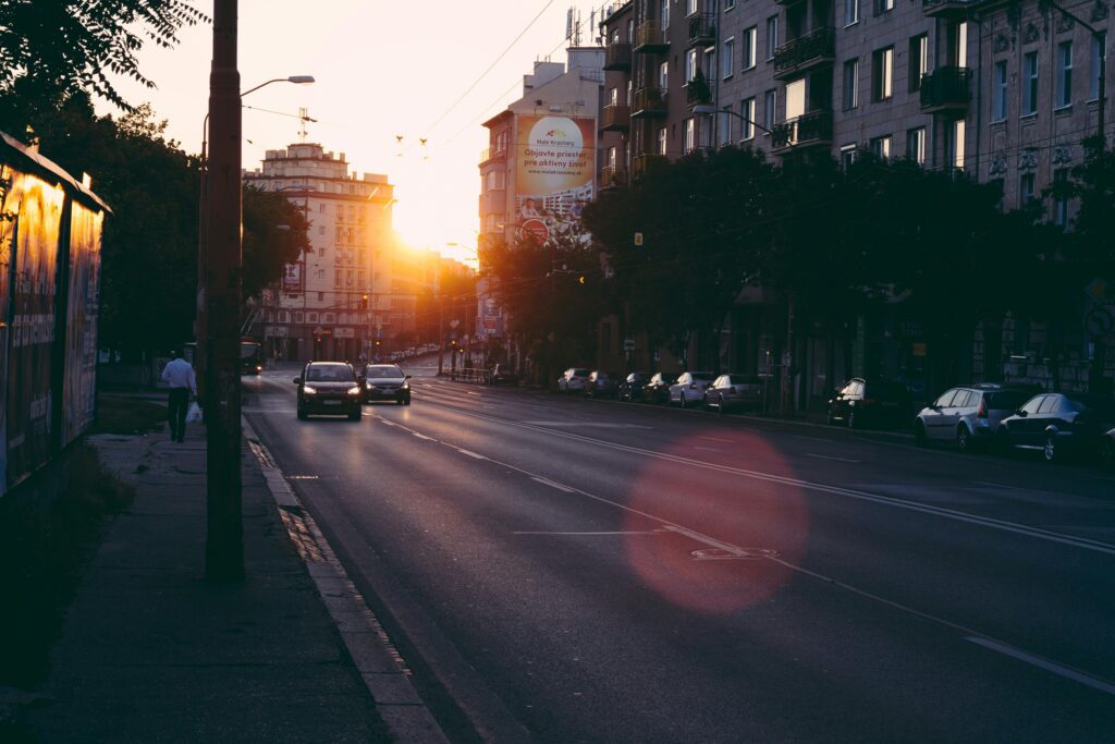 Urban street scene with cars and buildings during sunrise, capturing modern city life.