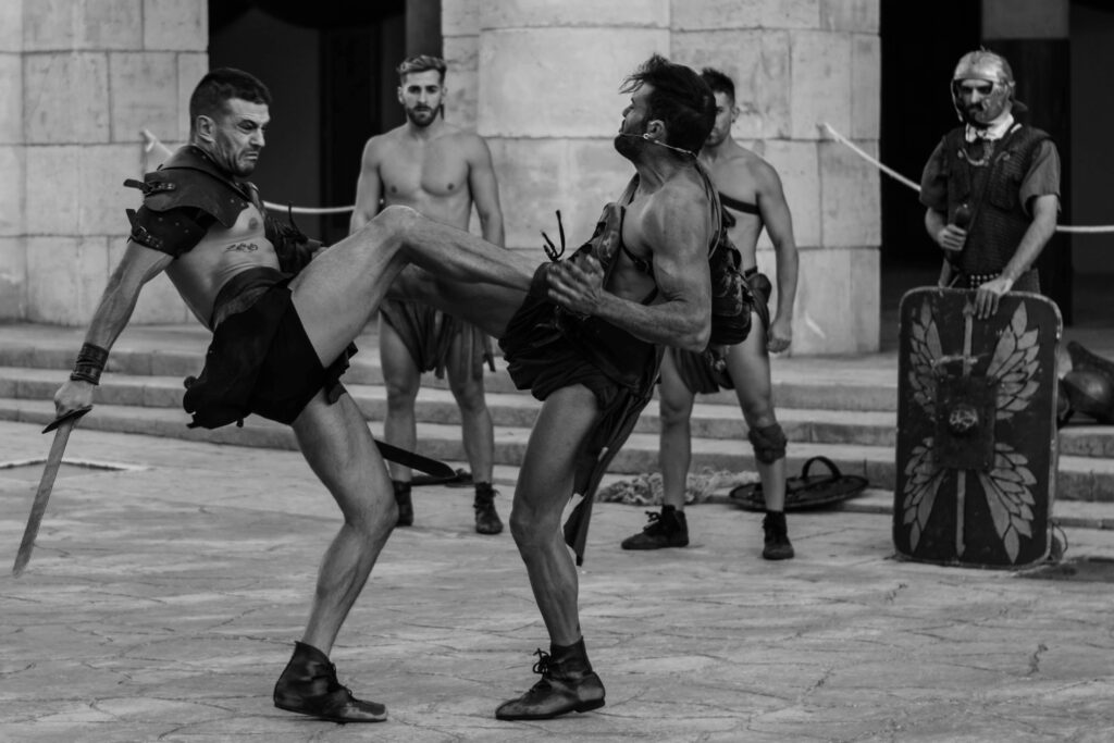 A dynamic black and white scene depicting gladiators engaging in an intense reenactment outdoors.