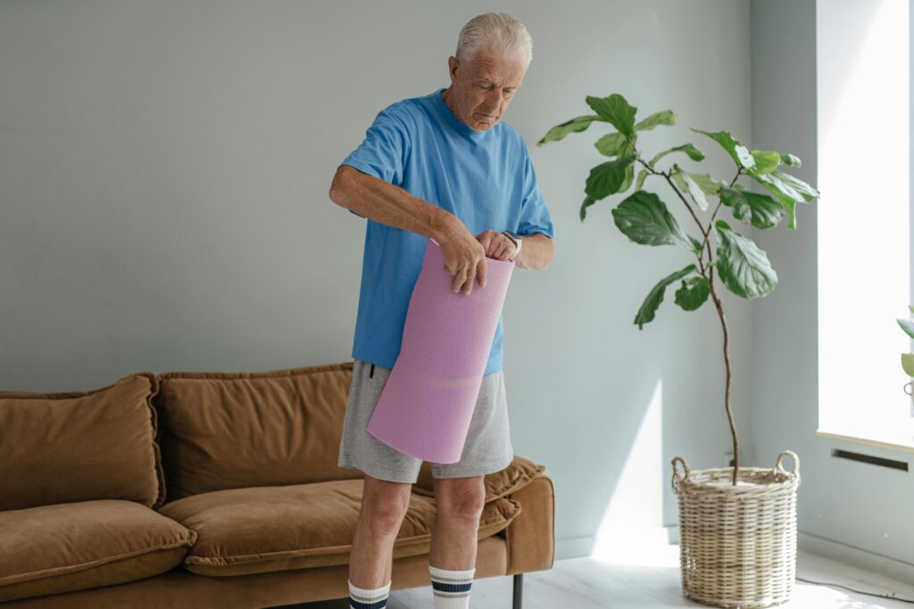 Elderly man in cozy room rolling out yoga mat for a healthy lifestyle workout.